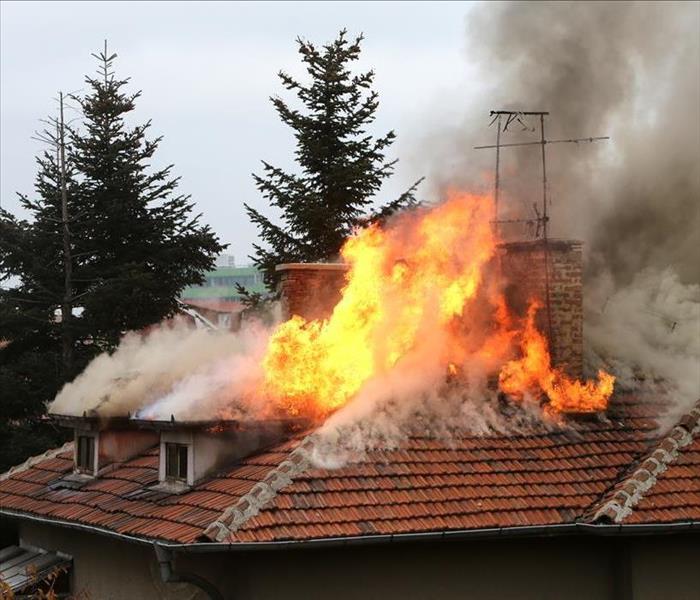Image of a house on fire, flames and smoke on top of the house.